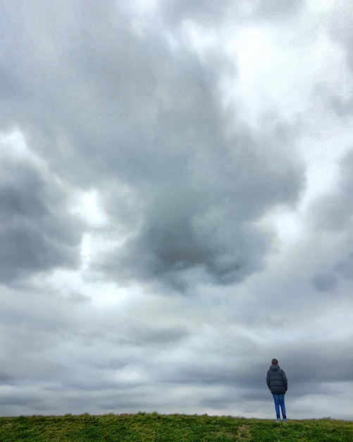 Achtergrondbeeld van een tiener die op het veld staat tegen een bewolkte lucht