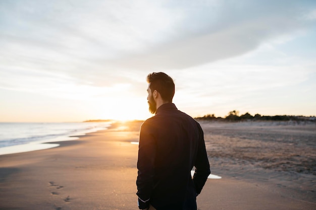 Achtergrondbeeld van een volwassen man die op het strand staat tegen een bewolkte hemel tijdens de zonsondergang