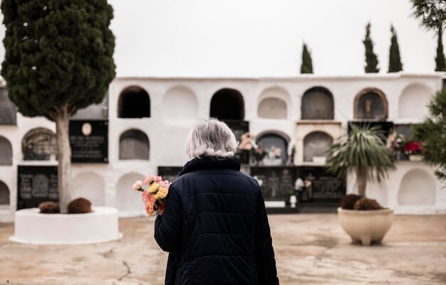 Foto achtergrondbeeld van een vrouw die bloemen vasthoudt en rouwt om haar familie op de begraafplaats van almeria, spanje