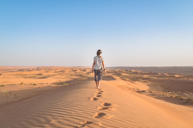 Achtergrondbeeld van een vrouw die in de woestijn loopt tegen een heldere lucht