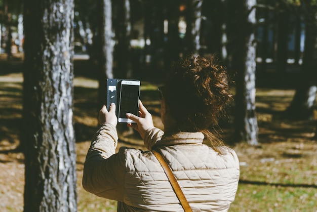 Foto achtergrondbeeld van een vrouw die met een mobiele telefoon in het bos fotografeert