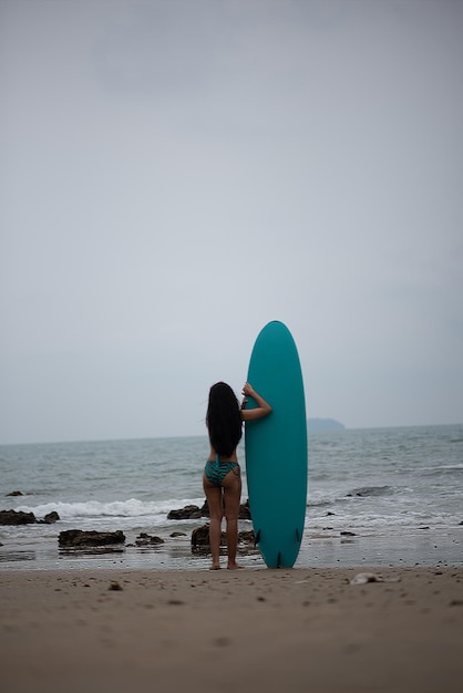 Foto achtergrondbeeld van een vrouw die met een surfplank op het strand tegen de lucht staat