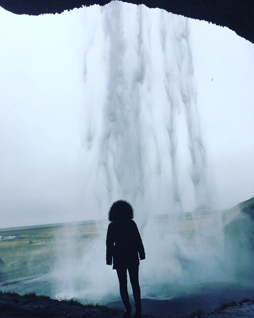 Foto achtergrondbeeld van een vrouw die naar een waterval kijkt terwijl ze in een grot staat