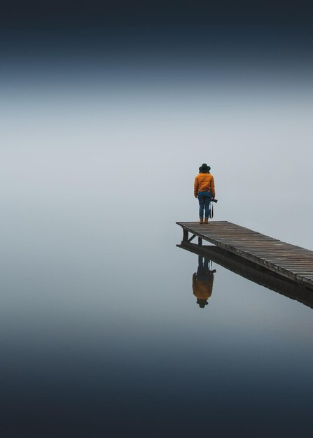 Foto achtergrondbeeld van een vrouw die op de pier over het meer tegen de lucht staat