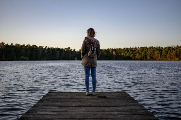 Foto achtergrondbeeld van een vrouw die op de pier over het meer tegen de lucht staat