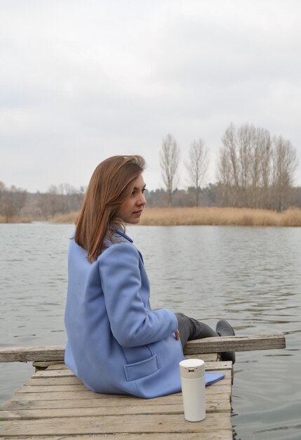 Foto achtergrondbeeld van een vrouw die op de pier tegen het meer zit