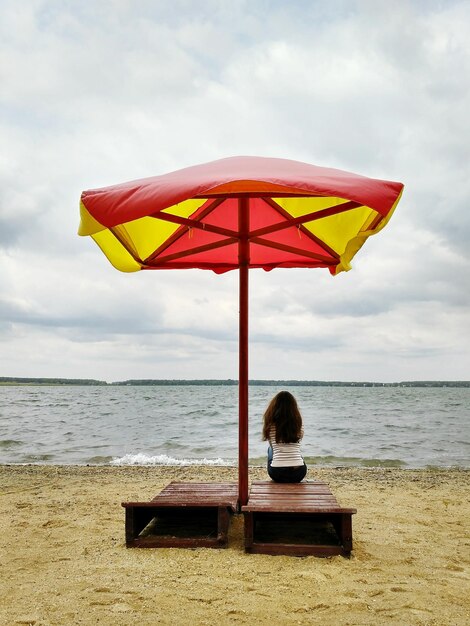 Foto achtergrondbeeld van een vrouw die op een ligstoel zit onder een parasol op het strand