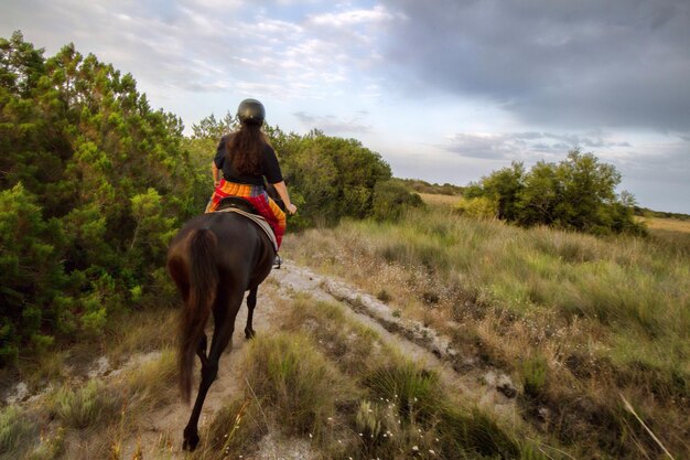 Foto achtergrondbeeld van een vrouw die op een paard rijdt op een veld tegen een bewolkte lucht