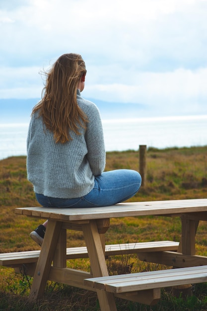 Foto achtergrondbeeld van een vrouw die op een picknicktafel tegen de lucht zit