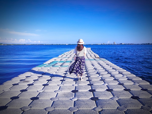 Foto achtergrondbeeld van een vrouw die op een pier bij de zee staat tegen een blauwe hemel