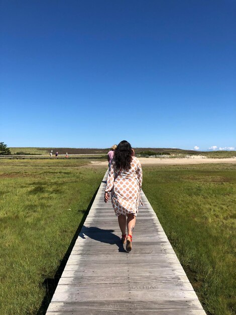 Foto achtergrondbeeld van een vrouw die op het veld loopt tegen een heldere lucht