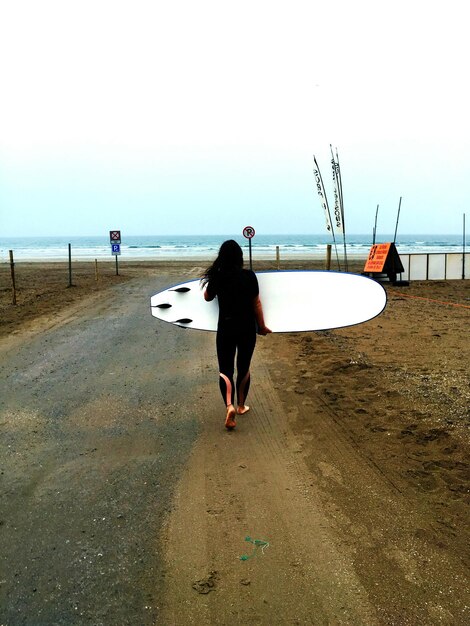 Foto achtergrondbeeld van een vrouw die tijdens de zonsondergang een surfplank op het strand draagt