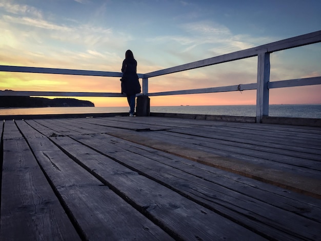 Foto achtergrondbeeld van een vrouw die tijdens de zonsondergang op een pier bij de zee staat