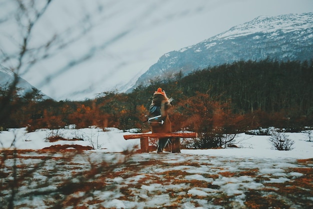 Foto achtergrondbeeld van een vrouw die warme kleding draagt terwijl ze op een bankje tegen de bergen zit