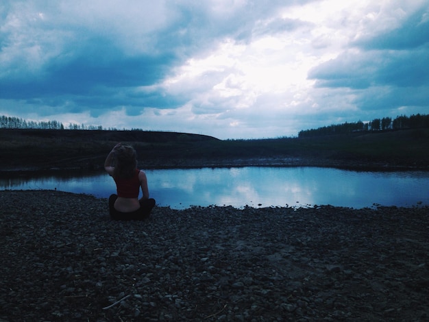 Foto achtergrondbeeld van een vrouw die zich ontspant aan de oever van het meer tegen een bewolkte lucht