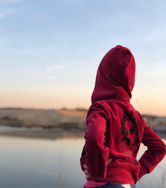 Foto achtergrondbeeld van een vrouw met een capuchon terwijl ze bij het meer staat tijdens de zonsondergang