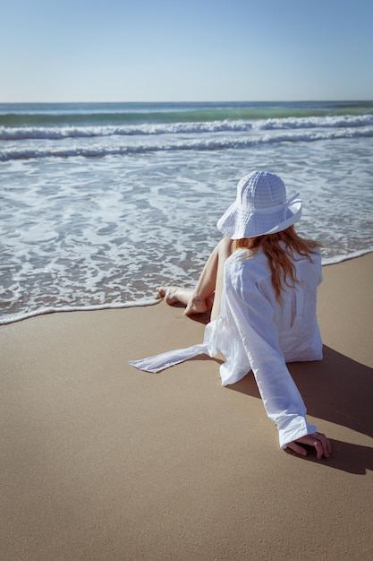 Achtergrondbeeld van een vrouw met een hoed die op het strand zit