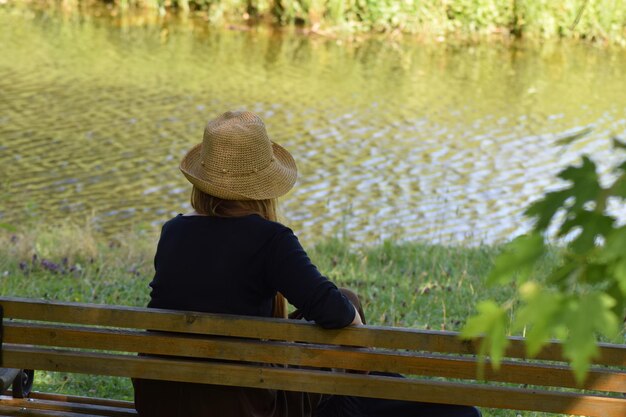 Achtergrondbeeld van een vrouw met een hoed terwijl ze op een bankje bij het meer zit