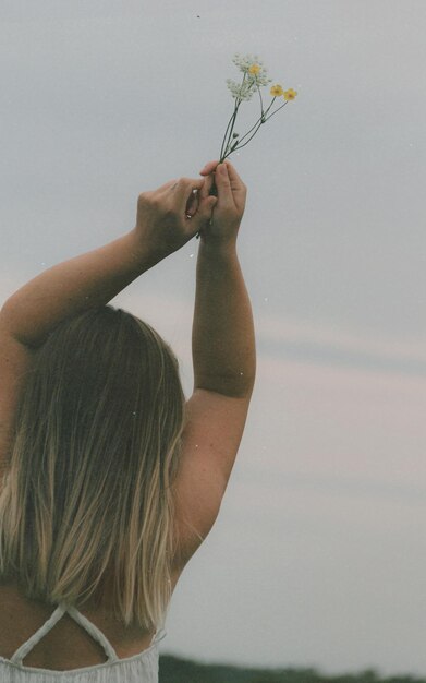 Foto achtergrondbeeld van een vrouw met een rode bloeiende plant tegen de lucht