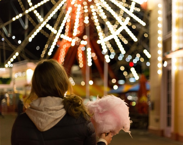 Achtergrondbeeld van een vrouw met suikerwatten tegen een verlicht reuzenwiel's nachts