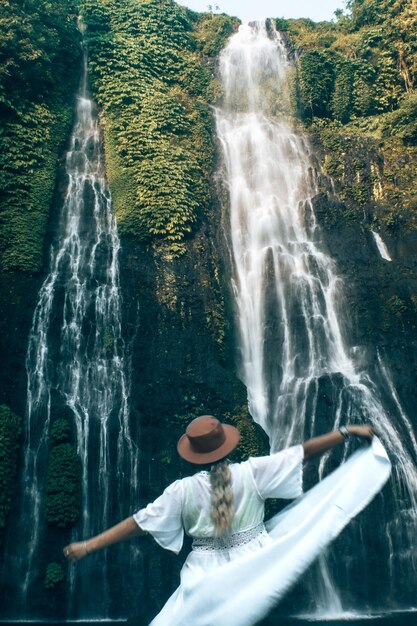 Foto achtergrondbeeld van een vrouw met uitgestrekte armen die naar een waterval kijkt