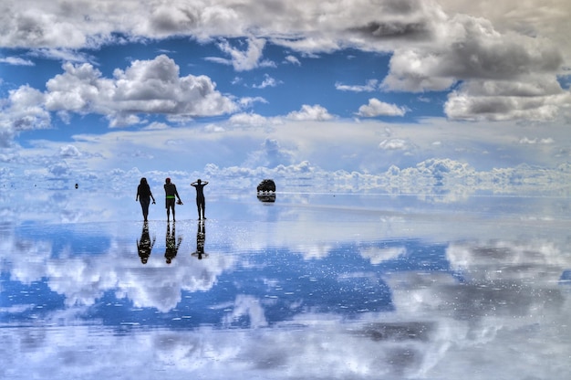 Achtergrondbeeld van vrienden die op een bevroren meer staan met de weerspiegeling van een bewolkte hemel