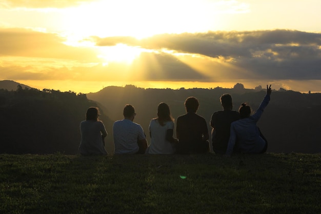 Achtergrondbeeld van vrienden die tijdens de zonsondergang op het veld tegen de lucht zitten