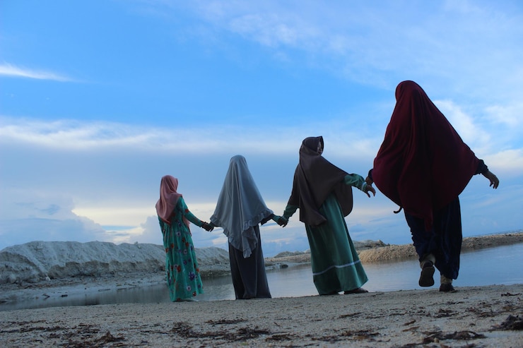 Foto achtergrondbeeld van vrouwen die hand in hand staan op het strand tegen de lucht