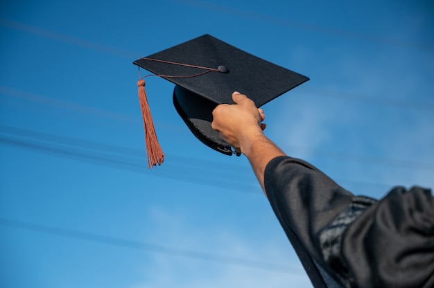 achterk bezichtiging, van, man, in, afstuderen, toga, vasthouden, pet, staand, tegen, hemel