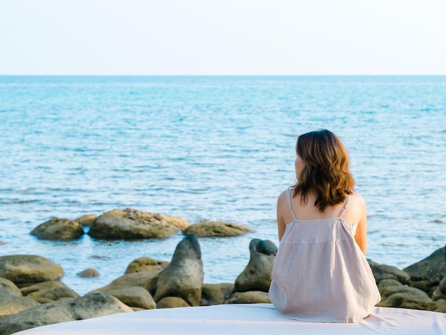 Achterkant van Aziatische vrouw in casual kleding zit in de zomer voor het strand en de rotskust