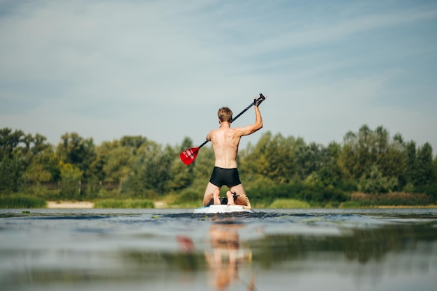 Achterkant van een jonge sportman roeit actief op de rivier op een sup board