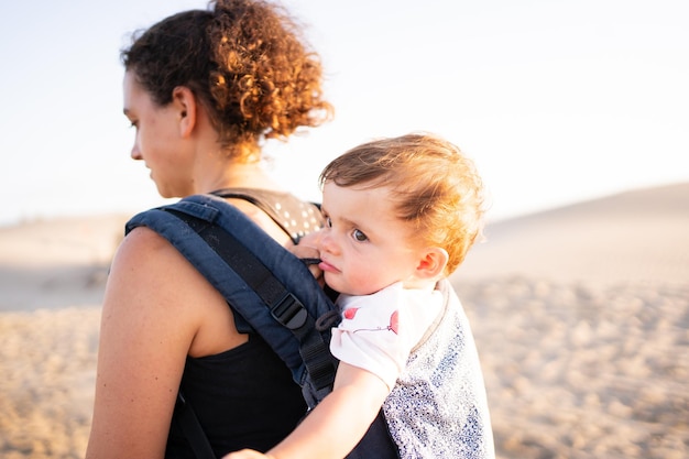 Achterkant van een vrouw die tijdens zonsondergang een baby in een draagzak draagt