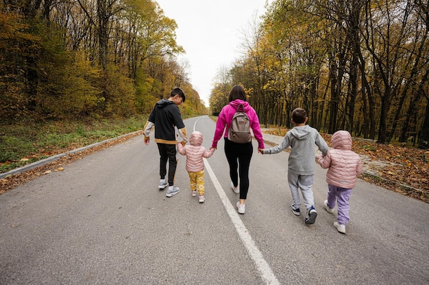 Achterkant van moeder met vier kinderen die op de weg rennen in het herfstbos