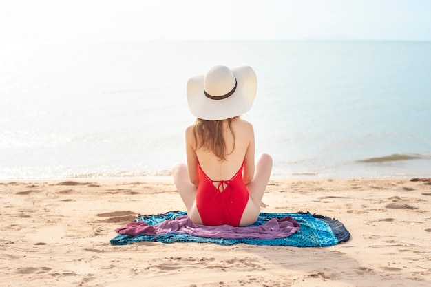 Achterkant van Mooie vrouw in rode zwembroek zit op het strand