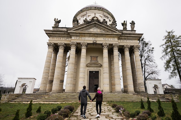 Achterkant van paar hand in hand tegen barokke rooms-katholieke kerk in Pidhirtsi Lviv Oblast Oekraïne