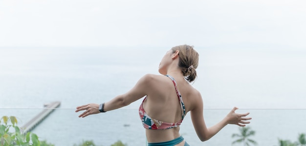 Achterkant van vrouw in zwembroek posten op het transparante glazen balkon met uitzicht op de oceaan.