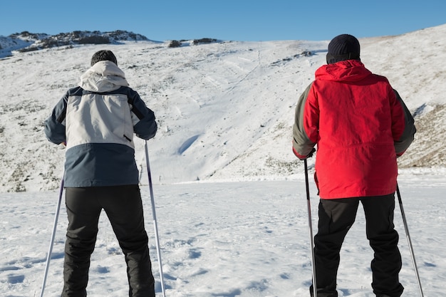 Achtermening van een paar met skistokken op sneeuw