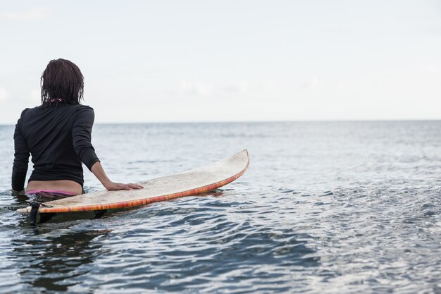 Achtermening van een vrouw met surfplank in het water