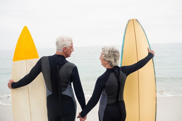 Achtermening van hoger paar met de hand van de surfplankholding op het strand