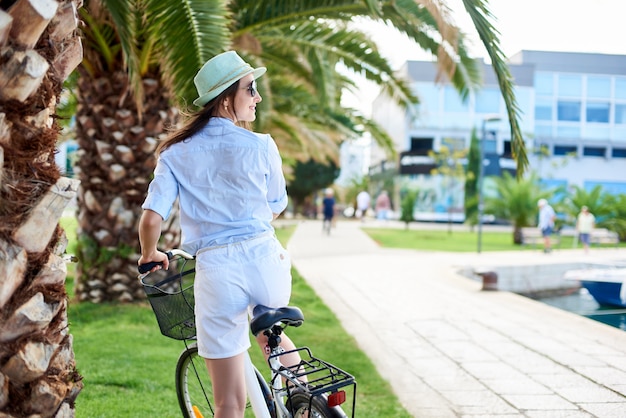 Achtermening van jonge gelukkige vrouw die een fiets berijden op groene palm op heldere zonnige dag