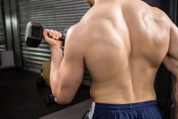 Achtermening van shirtless mens die zware domoren opheffen bij de crossfitgymnastiek