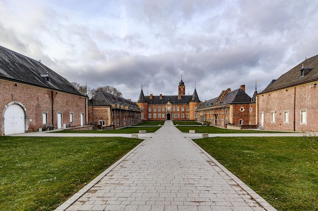 Achterste buitenpatio met recht geplaveid pad richting kasteel Alden Biesen op de achtergrond bakstenen muren en zadeldak 16e-eeuwse bewolkte dag met stormachtige bewolkte hemel in Bilzen, Limburg, België