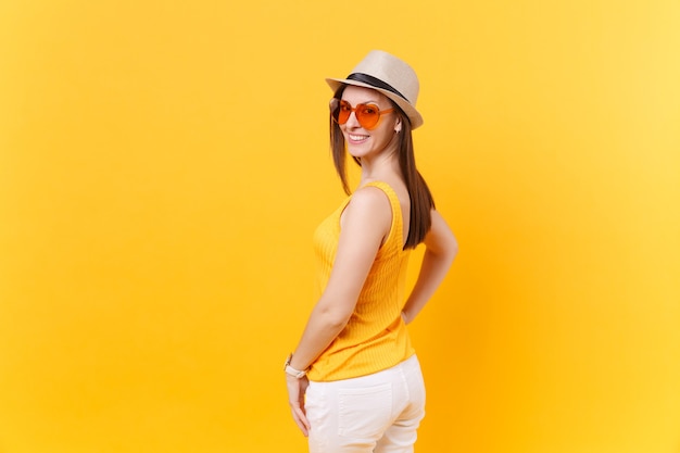Achterste portret weergave van jonge vrouw in stro zomer hoed, oranje bril op zoek terug, kopieer ruimte geïsoleerd op gele achtergrond. Mensen oprechte emoties, lifestyle concept. Reclame gebied.