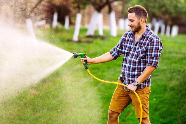 Achtertuin tuinieren details portret van tuinman die waterslang gebruikt en het gras en de planten water geeft