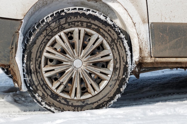 Achterwiel van vuile auto die zich in sneeuwclose-up bevindt