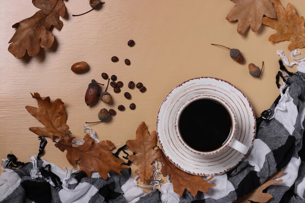 ベージュの背景に秋のオークの葉と市松模様のスカーフとどんぐりコーヒー。