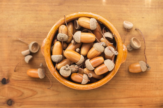 Acorns in a clay bowl on a wooden table in a top view