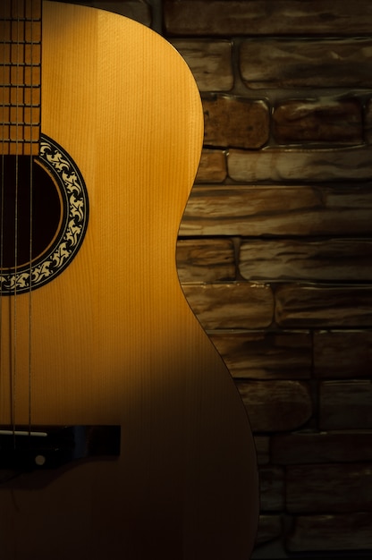 Acoustic guitar brick wall in the dark, a beam of light illuminates it.