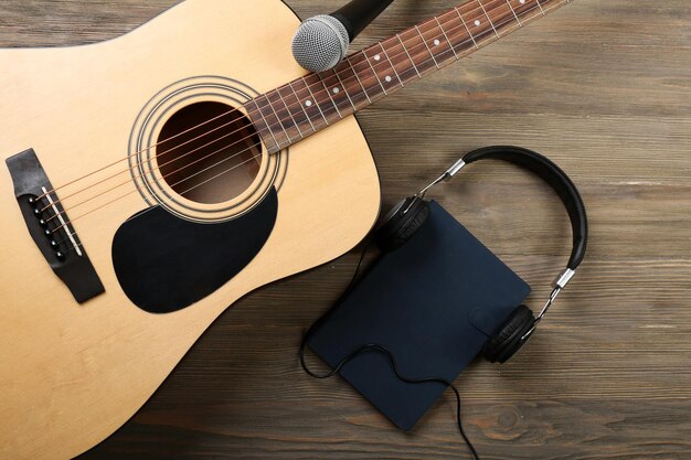 Acoustic guitar headphones notebook and microphone on wooden background close up