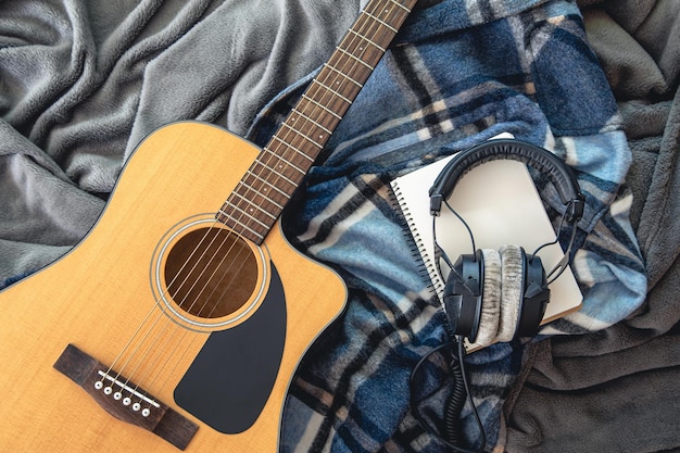 Acoustic guitar headphones and notepad on plaid background top view